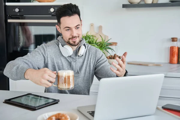 Adam evde sabah kahvesi içerken biriyle online görüşme yapıyor.