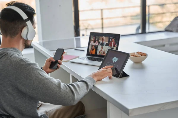 Mężczyzna noszący słuchawki przegląda swój laptop i dzwoni do klientów. — Zdjęcie stockowe