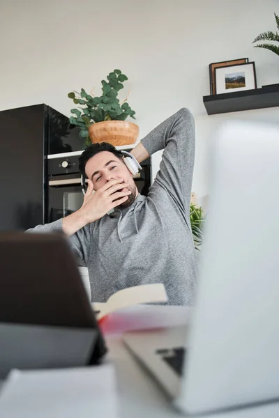 Trabajador hábil en bostezos auriculares y estiramiento mientras trabaja con computadora portátil en el hogar — Foto de Stock