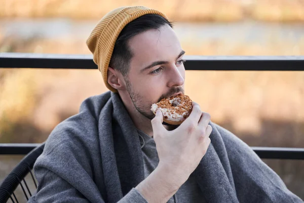 Homem da aparência caucasiana morde o pão enquanto olha para longe — Fotografia de Stock