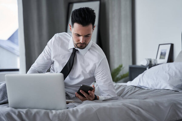 Busy man looking at the smartphone and checking email while using his laptop