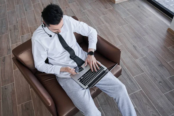 Evcil pantolonlu ve resmi tişörtlü bir adam koltukta oturuyor ve dizüstü bilgisayarında daktilo yazıyor. — Stok fotoğraf