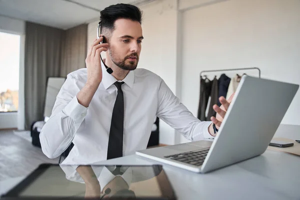 Administrador de calma corrigiendo sus auriculares mientras está sentado delante de la computadora portátil — Foto de Stock