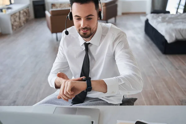 Manager im Headset blickt vor dem Laptop auf die Armbanduhr — Stockfoto