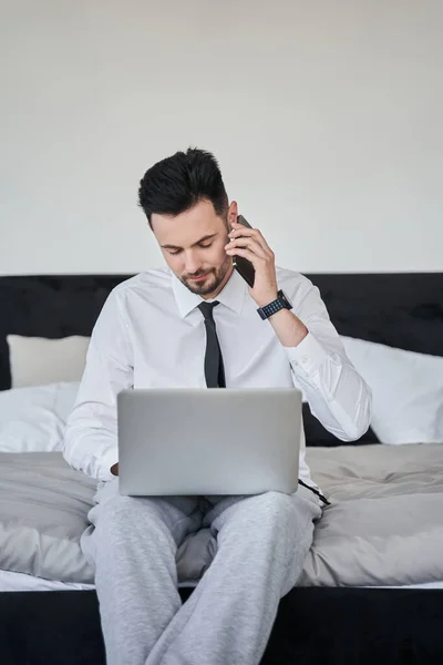 Empresario sentado en la cama y conversando en el smartphone — Foto de Stock