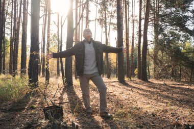 Yaşlı yürüyüşçü ağaçların arasında güneşin doğuşunun tadını çıkarırken kollarını açtı.