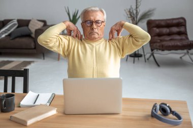 Yaşlı adam omuzlarını gösteriyor ya da egzersiz yapıyor.