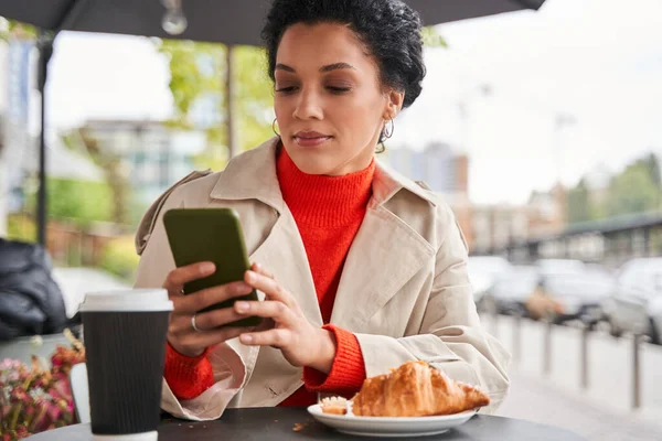 Mujer mirando la pantalla del teléfono inteligente mientras está sentada en la mesa — Foto de Stock