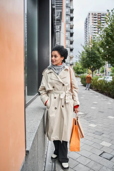 Multirazziale signora guardando vetrina mentre in piedi con shopping bags dopo il suo shopping — Foto Stock