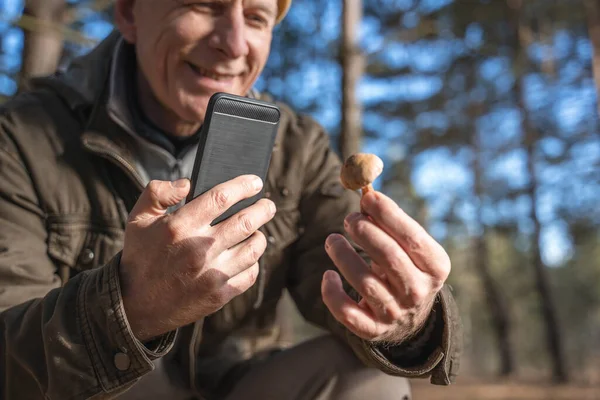 Hombre leyendo algo en su teléfono inteligente y sosteniendo hongo en su mano — Foto de Stock