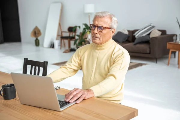 Sérieux homme âgé utilisant un ordinateur portable à la maison — Photo
