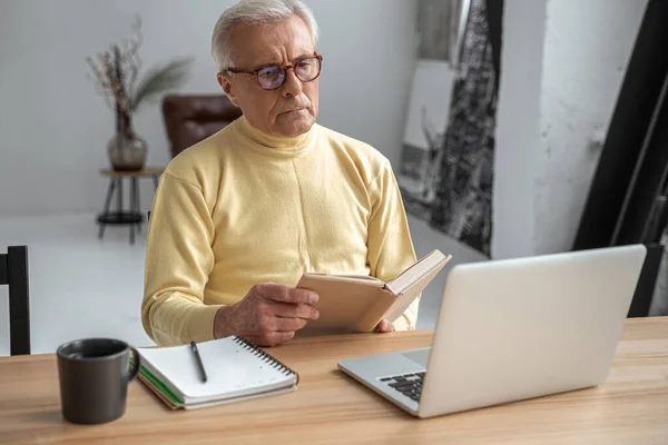 Mindful man in bril lezen verhalenboek aandachtig terwijl zitten aan de tafel — Stockfoto