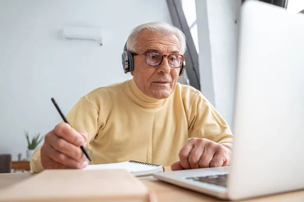 Концентрований старший дід дивиться онлайн-вебінар і пише нотатки — стокове фото