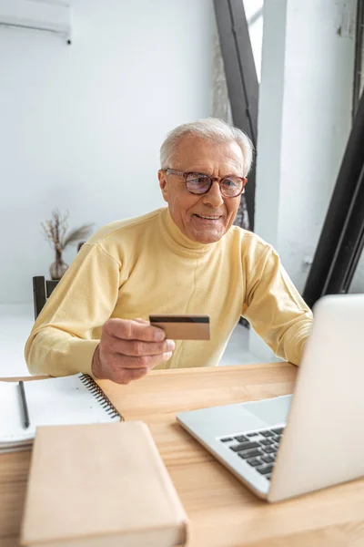 Gözlüklü olgun bir adam kredi kartıyla online alışveriş yapıyor. — Stok fotoğraf
