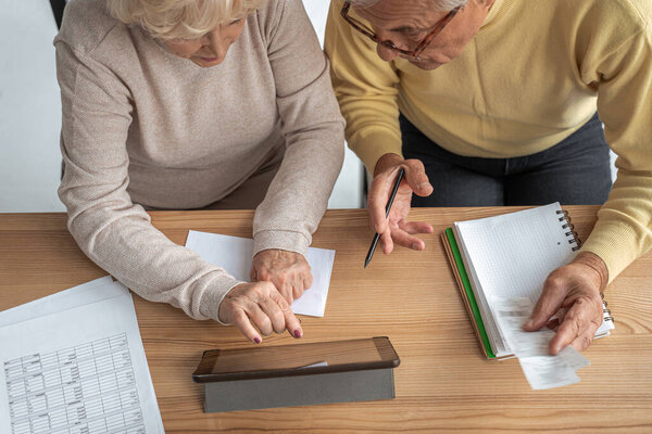 Focused senior husband and wife sitting at table at home and looking at tablet screen