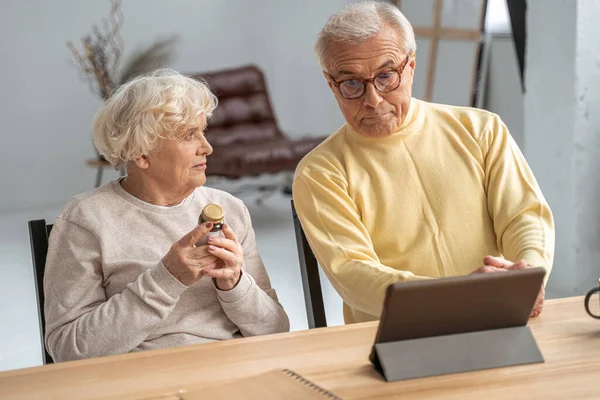 Gammal par undersöka burk med piller när du sitter vid bordet och har samtal — Stockfoto