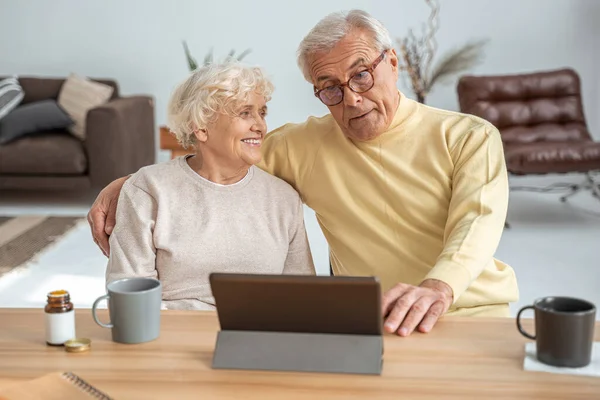Pasangan dewasa merangkul sambil melihat tablet dengan senyum gembira — Stok Foto