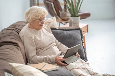 Online webinar izlerken evde dijital tablet kullanan kıdemli bir kadın