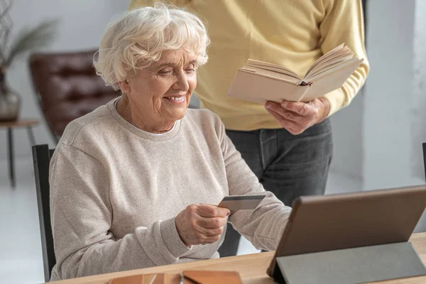 Mujer jubilada usando tarjeta de crédito para ir de compras en línea mientras está sentada frente a la tableta — Foto de Stock