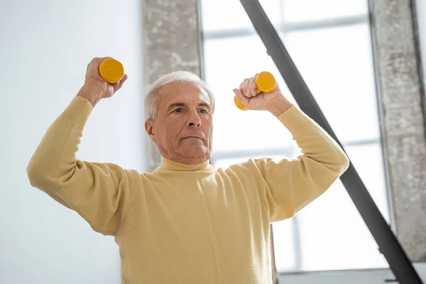 Enerjik, olgun, gri saçlı, turuncu halterli bir adam evde egzersiz yapıyor. — Stok fotoğraf