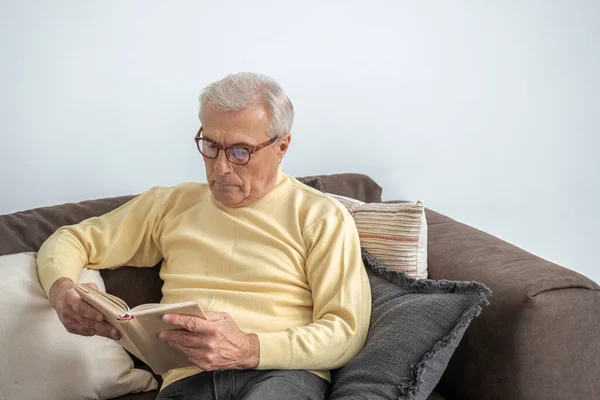 Thoughtful aged man reading favorite literature at cozy home — Stock Photo, Image