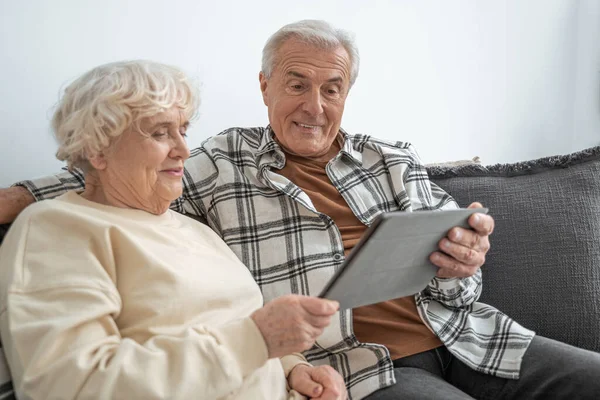 Старша пара сидить на дивані вдома і має відеодзвінок — стокове фото