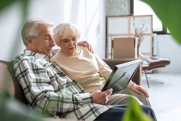 Modent, kaukasisk par som omfavner ømt når de sitter i sofaen – stockfoto