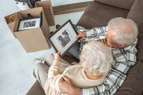 Kobieta i mężczyzna patrząc na zdjęcie w ramce podczas objęcia w nowym domu na kanapie — Zdjęcie stockowe