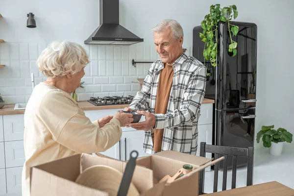 Oudere vrouw neemt bord van haar oudere man tijdens het uitpakken van dozen — Stockfoto