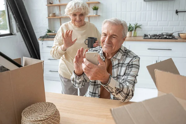 Aposentadoria homem segurando smartphone e acenando enquanto conversa com alguém — Fotografia de Stock