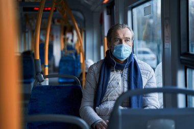 Mature male person in protective mask wearing earphones listening music
