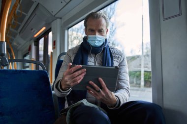 Elderly man wearing protective mask spending time with his tablet