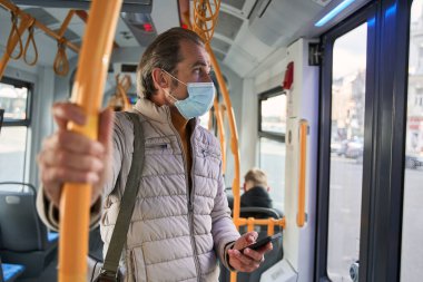Male person looking at the window and holding his smartphone while enjoying of the views