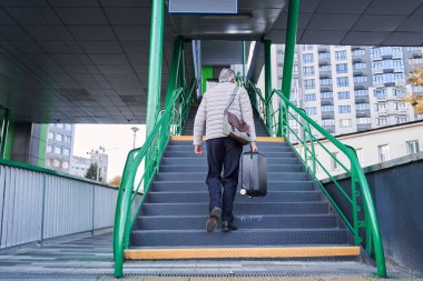 Mature male going up stairs while rising to the bus or railway station with his suitcase