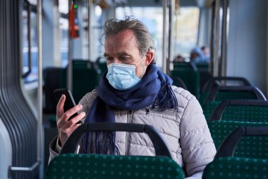 Modern pensioner sitting at the bus or tram and holding smartphone at his hands