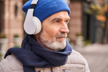 Calm senior bearded man looking away while listening music