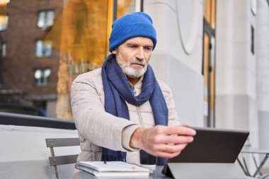 Senior joyful man entertaining with gadget in cafe