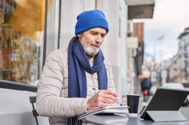 Mature man making notes and drinking coffee during the working