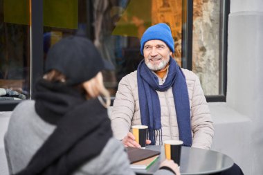 Man drinking coffee and chatting while sitting at the cafe with his female friend