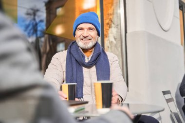 Overjoyed man smiling toothy to his friend while drinking coffee together at the street