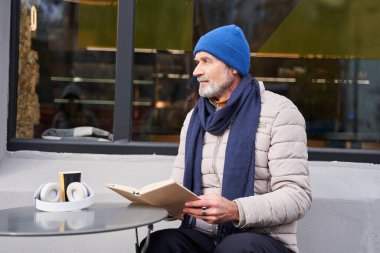 Calm bearded man sitting in cafe with coffee and reading a book