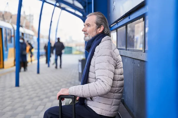 Retirement man with luggage sitting on the bus station while waiting for his transport — Foto Stock