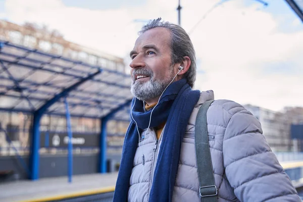 Vieux mâle debout dehors et écoutant sa musique préférée en attendant le train — Photo