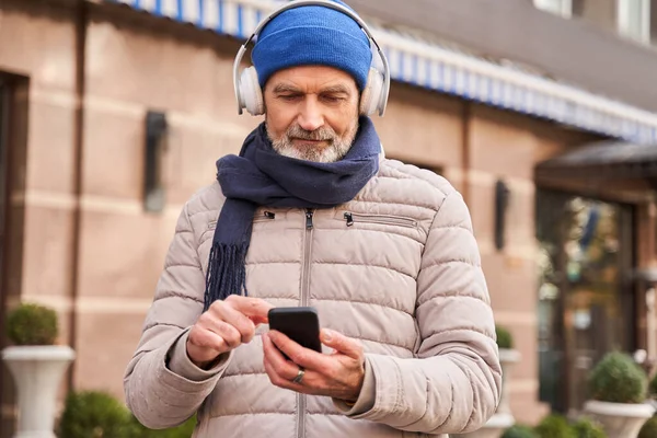 Retirement man wearing headphones standing at the street and listening music