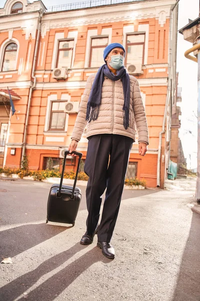 Retirement man wearing protective mask at his face holding baggage — 图库照片