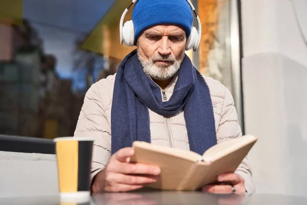 Agréable homme barbu mature portant des écouteurs sans fil assis au café — Photo