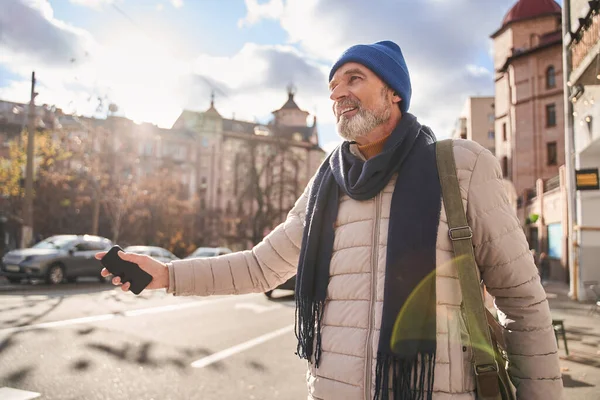 Grey haired mature man keeping his hand up while getting a taxi