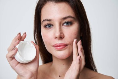 Elinde nemlendirici kremi olan ve yanağına sürmeye hazırlanan bir kadın.
