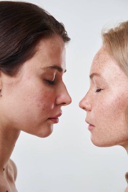 Kapalı gözlü ve farklı ten renginde farklı kızlar birbirlerine yakın duruyorlar.