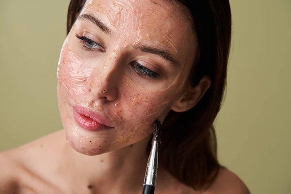 Mujer agradable aplicación de máscaras de belleza durante el uso de cepillo cosmético y posando —  Fotos de Stock